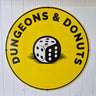 Circular sign with 'Dungeons & Donuts' and a dice graphic on a white wall.